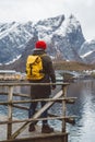 Young man with a backpack standing on a wooden pier the background of snowy mountains and lake. Place for text or advertising Royalty Free Stock Photo