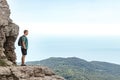 Young man with a backpack on top of cliff enjoying view of nature. Mountains and sea Royalty Free Stock Photo