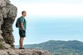 Young man with a backpack on top of cliff enjoying view of nature. Mountains and sea