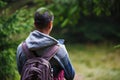 A young man with a backpack in the woods looking at the phone-a view from the back. Royalty Free Stock Photo