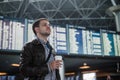 Young man with a bag in airport near flight timetable holding cup of coffee Royalty Free Stock Photo