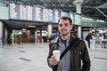 Young man with a bag in airport near flight timetable holding cup of coffee Royalty Free Stock Photo