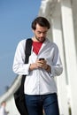 Young man with bag walking and sending text message outdoors Royalty Free Stock Photo