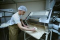 Young man baker standing at a dough forming machine and forming dough for baking baguette. Brovary, Ukraine