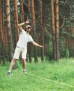 young man balancing his arms walk on a loose rope tied between two trees, male training slack rope walking, slacklining outdoors