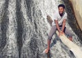 Young man barefoot in river sitting on tree trunk waterfalls