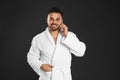 Young man in bathrobe talking on mobile phone against  background Royalty Free Stock Photo