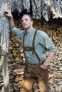 Young man in bavarian lederhosen in front of firewood