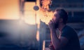 Young man with beard on blurry background sunset sky, making soap bubbles smoke inside with the aid of vape