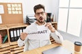 Young man with beard breaking contract paper at the office in shock face, looking skeptical and sarcastic, surprised with open Royalty Free Stock Photo