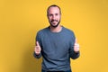 Young man with beard and casual clothing giving thumbs up as a gesture of approval with smiling and happy and expression on yellow Royalty Free Stock Photo