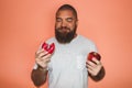 Young man with beard is choosing a fatty sugar donut instead of a healthy red apple Royalty Free Stock Photo