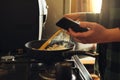 Young man with beard cooking dinner and using his smart phone at the kitchen. Royalty Free Stock Photo