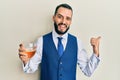 Young man with beard drinking a glass of white wine pointing thumb up to the side smiling happy with open mouth Royalty Free Stock Photo