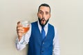Young man with beard drinking a glass of white wine scared and amazed with open mouth for surprise, disbelief face Royalty Free Stock Photo