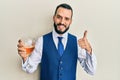 Young man with beard drinking a glass of white wine smiling happy and positive, thumb up doing excellent and approval sign Royalty Free Stock Photo