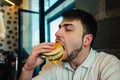 A young man with a beard eating a burger at the restaurant and enjoying the taste Royalty Free Stock Photo