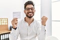 Young man with beard holding covid record card screaming proud, celebrating victory and success very excited with raised arms