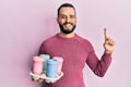 Young man with beard holding tray with take away coffee smiling with an idea or question pointing finger with happy face, number