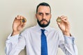 Young man with beard holding virtual currency ethereum coin and bitcoin skeptic and nervous, frowning upset because of problem