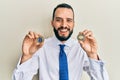 Young man with beard holding virtual currency ethereum coin and bitcoin smiling and laughing hard out loud because funny crazy