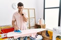 Young man with beard ironing clothes at home smelling something stinky and disgusting, intolerable smell, holding breath with Royalty Free Stock Photo