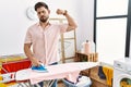 Young man with beard ironing clothes at home strong person showing arm muscle, confident and proud of power Royalty Free Stock Photo