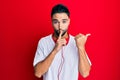 Young man with beard listening to music using headphones asking to be quiet with finger on lips pointing with hand to the side Royalty Free Stock Photo