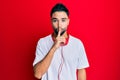 Young man with beard listening to music using headphones asking to be quiet with finger on lips Royalty Free Stock Photo