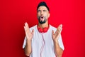 Young man with beard listening to music using headphones celebrating mad and crazy for success with arms raised and closed eyes Royalty Free Stock Photo