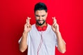 Young man with beard listening to music using headphones gesturing finger crossed smiling with hope and eyes closed Royalty Free Stock Photo