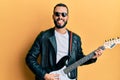 Young man with beard playing electric guitar sticking tongue out happy with funny expression Royalty Free Stock Photo