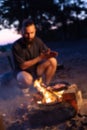 A young man with a beard prepares a dish of bacon with scrambled eggs on a fire. Cooking and outdoor recreation in summer, blurry Royalty Free Stock Photo