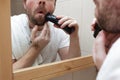 Young man with a beard shave stubble with electric razor.