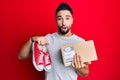 Young man with beard taking casual red shoes from box afraid and shocked with surprise and amazed expression, fear and excited