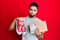 Young man with beard taking casual red shoes from box depressed and worry for distress, crying angry and afraid