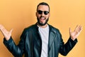 Young man with beard wearing black leather jacket and sunglasses celebrating victory with happy smile and winner expression with Royalty Free Stock Photo