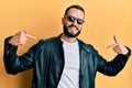Young man with beard wearing black leather jacket and sunglasses looking confident with smile on face, pointing oneself with Royalty Free Stock Photo