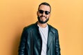 Young man with beard wearing black leather jacket and sunglasses looking positive and happy standing and smiling with a confident Royalty Free Stock Photo