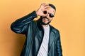 Young man with beard wearing black leather jacket and sunglasses smiling happy doing ok sign with hand on eye looking through Royalty Free Stock Photo