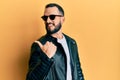 Young man with beard wearing black leather jacket and sunglasses smiling with happy face looking and pointing to the side with Royalty Free Stock Photo