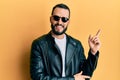 Young man with beard wearing black leather jacket and sunglasses smiling happy pointing with hand and finger to the side Royalty Free Stock Photo