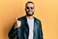 Young man with beard wearing black leather jacket and sunglasses smiling happy and positive, thumb up doing excellent and approval Royalty Free Stock Photo