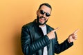 Young man with beard wearing black leather jacket and sunglasses smiling and looking at the camera pointing with two hands and Royalty Free Stock Photo