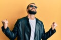 Young man with beard wearing black leather jacket and sunglasses very happy and excited doing winner gesture with arms raised, Royalty Free Stock Photo