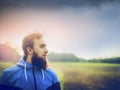 Young man with a beard wearing a blue jacket and in profile against green field and sky Royalty Free Stock Photo