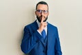 Young man with beard wearing business suit and tie asking to be quiet with finger on lips Royalty Free Stock Photo