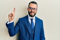 Young man with beard wearing business suit and tie showing and pointing up with finger number one while smiling confident and Royalty Free Stock Photo