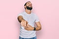 Young man with beard wearing casual white t shirt laughing at you, pointing finger to the camera with hand over body, shame Royalty Free Stock Photo