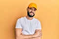 Young man with beard wearing yellow cap happy face smiling with crossed arms looking at the camera